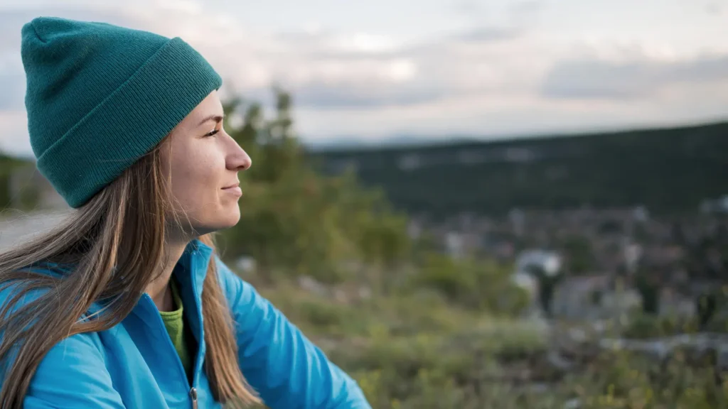Side view of a woman wearing a blue beanie, sitting outdoors and enjoying the view, representing healthy habits and relaxation, essential for maintaining good oral hygiene.