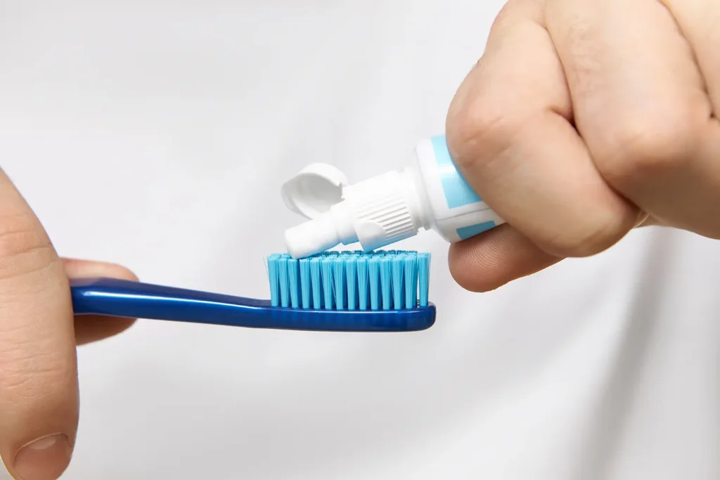 Close-up of a person squeezing toothpaste onto a blue toothbrush, emphasizing the importance of brushing your teeth for effective oral hygiene.