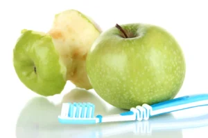 Green apples with a toothbrush, showcasing healthy foods that contribute to good oral health by naturally cleaning teeth and stimulating gums.