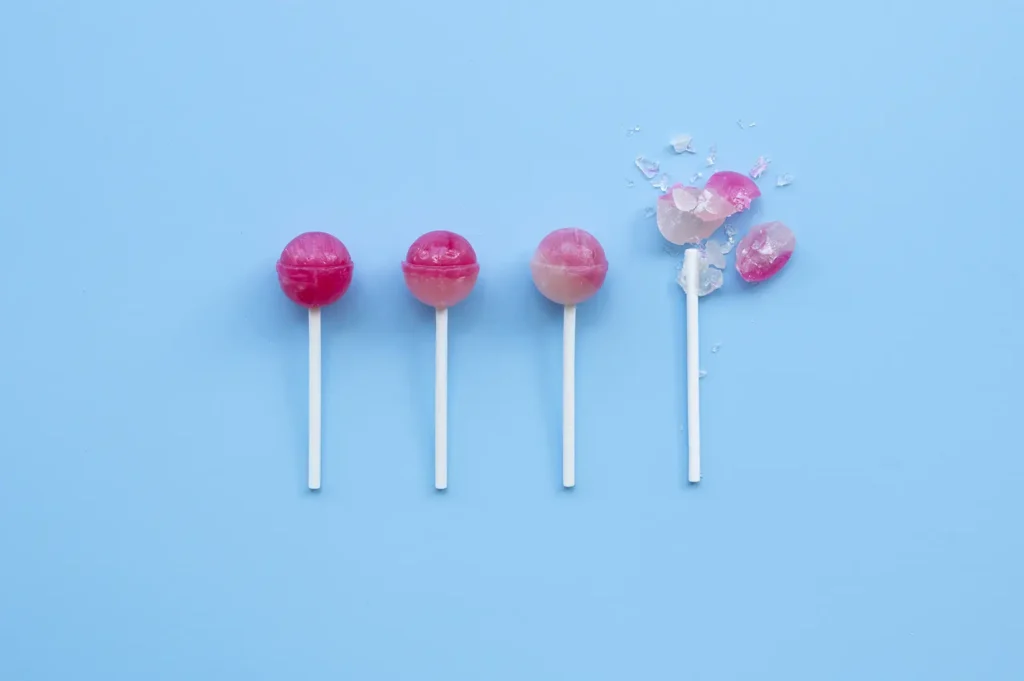 A row of colorful lollipops on a blue background, illustrating how sugary treats can negatively impact oral health compared to healthy foods.