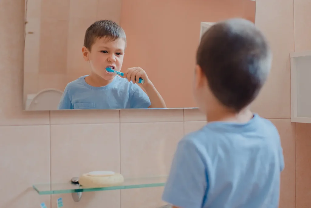 young boy brushing teeth in front of mirror demonstrating keeping teeth healthy and practicing oral hygiene