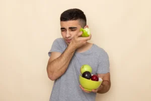 Man experiencing teeth sensitivity while biting an apple, holding his jaw in pain, illustrating why my teeth hurt.