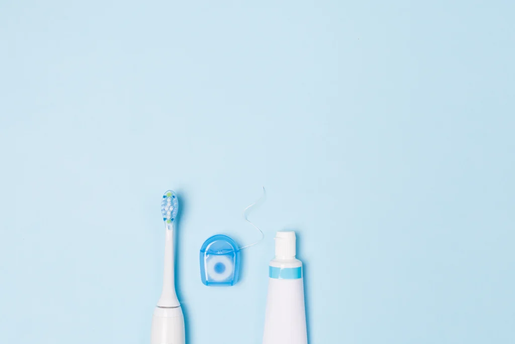 Electric toothbrush, dental floss, and toothpaste arranged on a light blue background, highlighting oral hygiene practices recommended by Legacy Smiles to complement dental inlays.